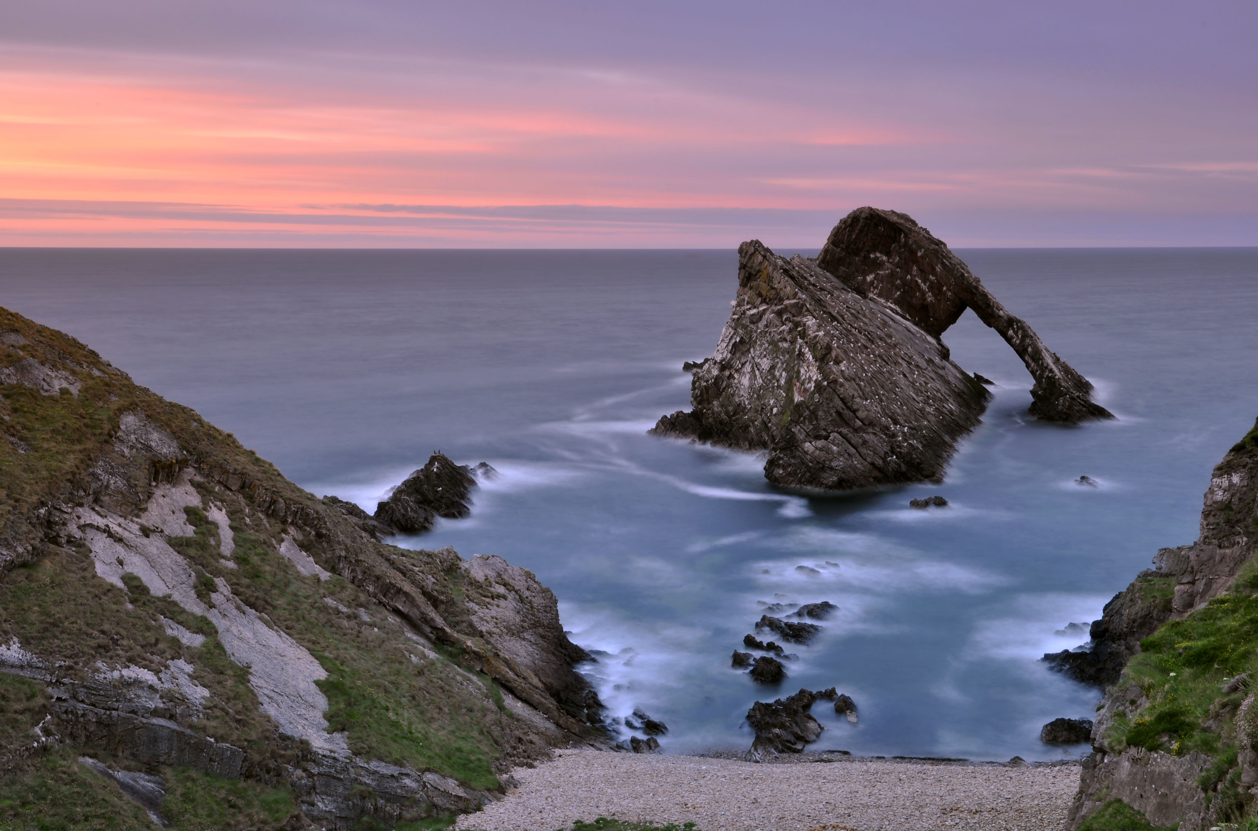 Bow Fiddle Rock in Moray sitting against purple and pink sunset over the sea